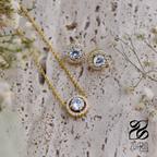 Gold necklace and earrings with clear stones on a textured surface with flowers.