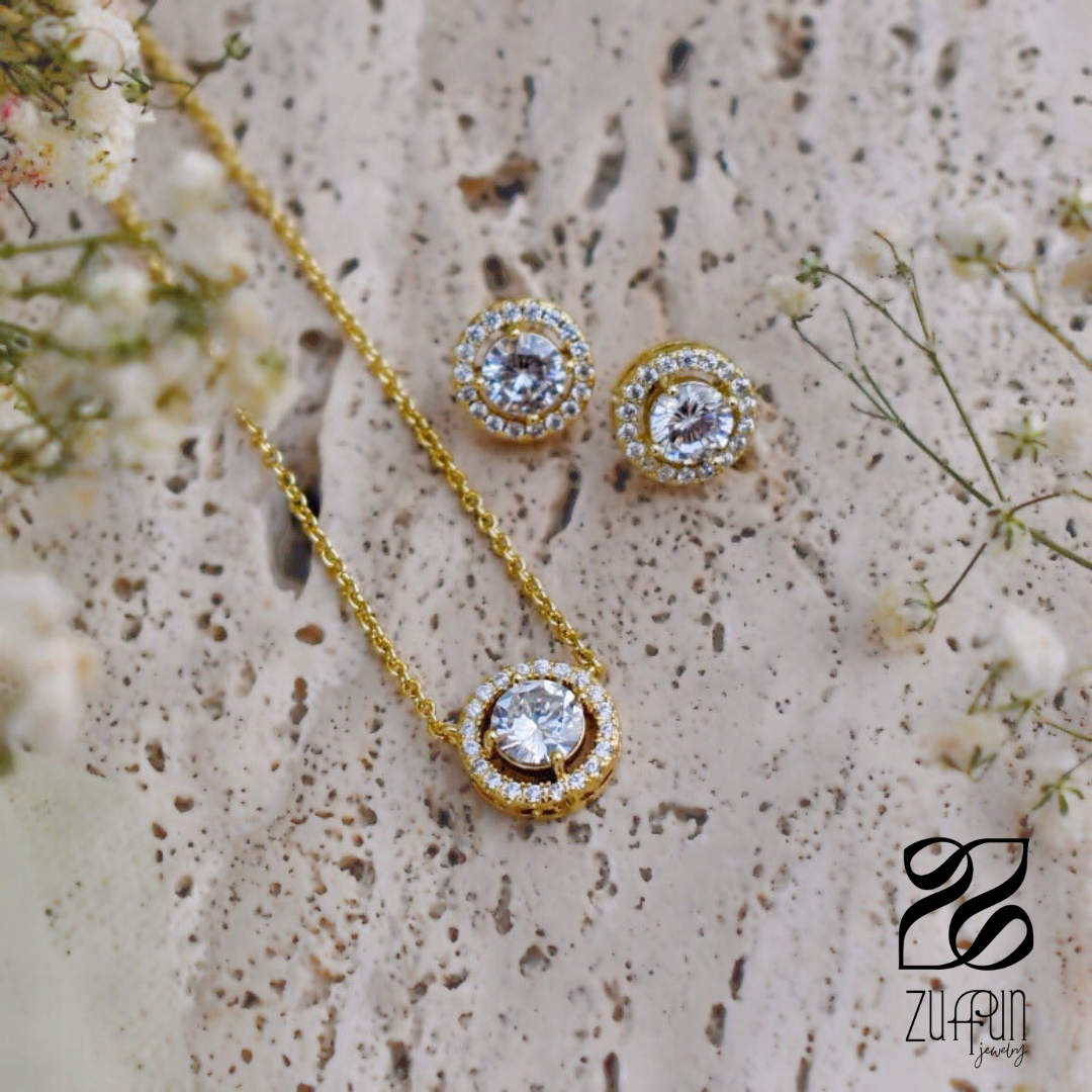 Gold necklace and earrings with clear stones on a textured surface with flowers.