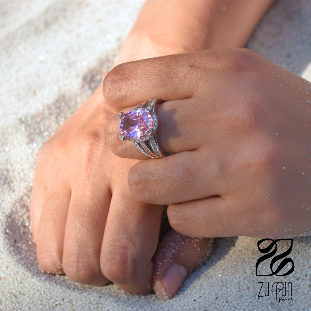 Hand wearing a pink gemstone ring on a sandy surface with Zulfur branding.