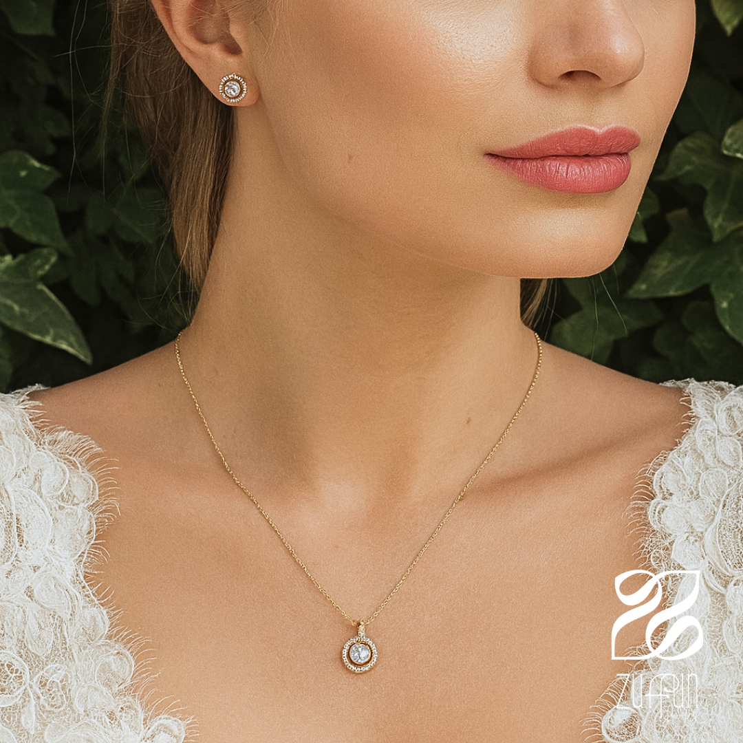 Close-up of a woman wearing a gold necklace with a pendant, earrings, and a white lace garment against a green leafy background.