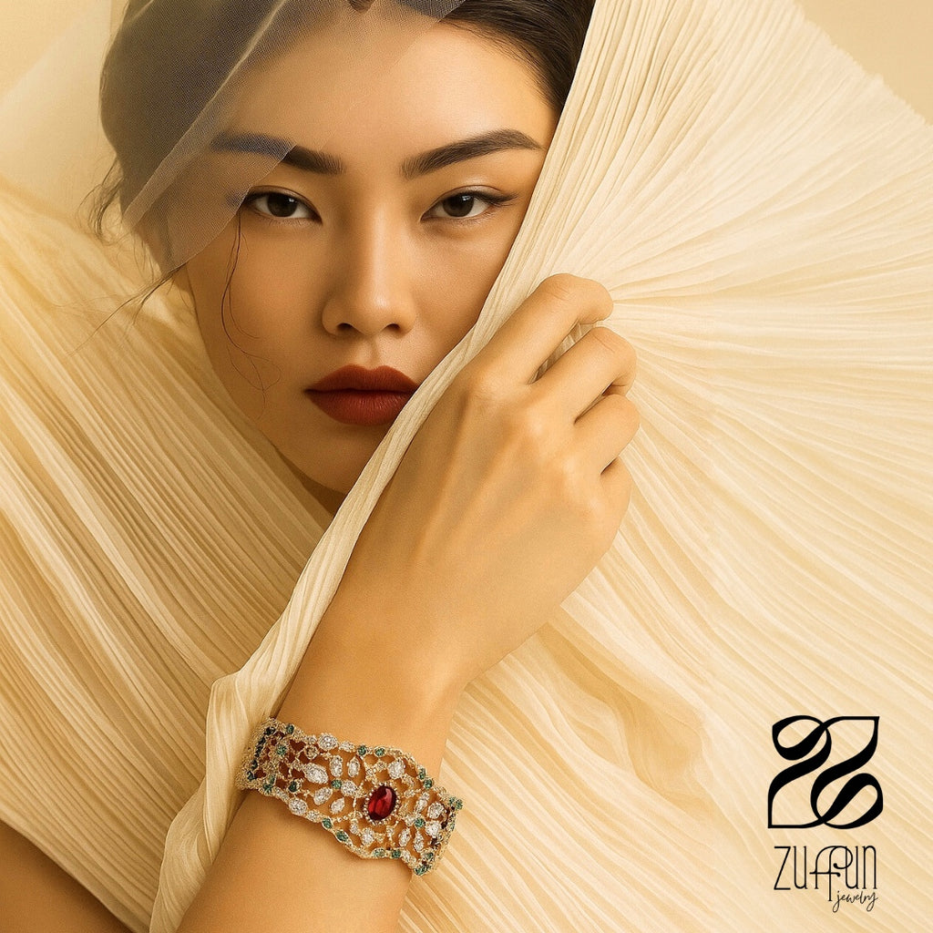 Woman wearing a zircon bracelet with a red and green zircons, holding a beige fabric, with Zuffun jewelry logo.